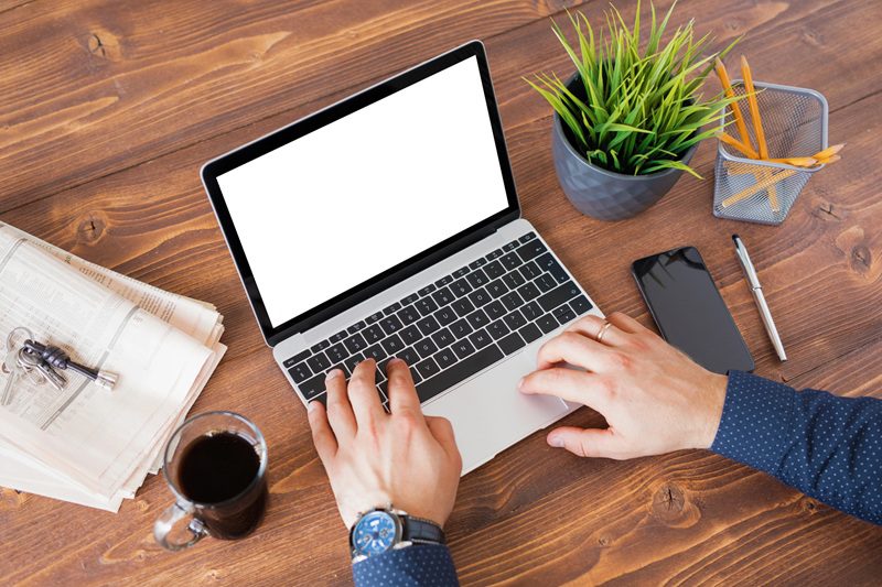 osoba pisząca na laptopie na biurku z telefonem, kawą i ołówkami