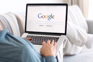 mężczyzna siedzący na kanapie i trzymający laptop z włączoną stroną Google