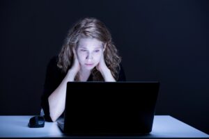młoda kobieta zmartwiona wpatrzona w świecący ekran laptopa
