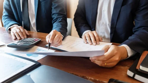 dwóch mężczyzn siedzących przy biurku i omawiających dokumenty prawne