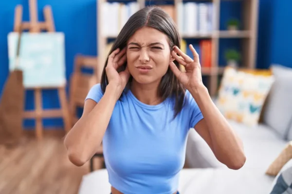 kobieta zatykająca uszy z bólu stojąca w salonie