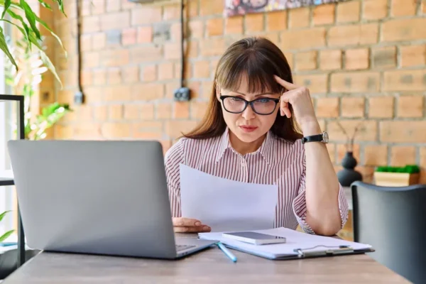 kobieta w okularach siedząca przy laptopie i czytająca dokument