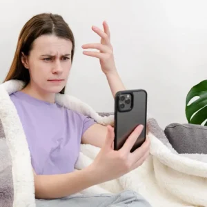 zmartwiona kobieta patrząca w ekran trzymanego w dłoni smartfona