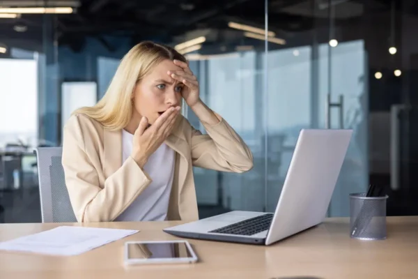 zdenerwowana kobieta w garniturze patrząca z niepokojem w ekran laptopa