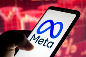 Dłoń trzymająca telefon z wyświetlonym logo Meta na tle czerwonego, rozmazanego wykresu, symbolizującego kryzys lub negatywne emocje w sieci.