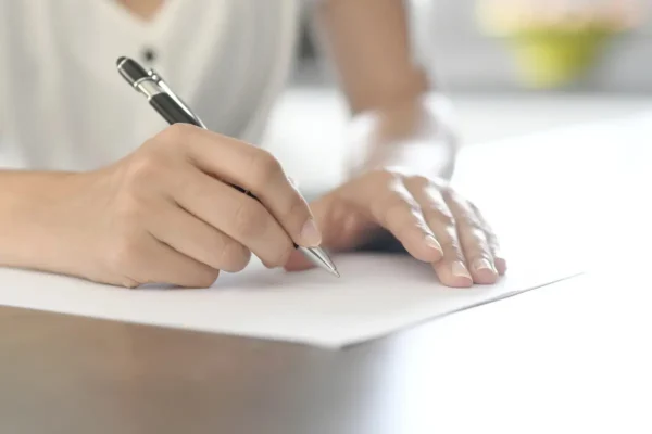 kobiece dłonie podpisujące dokument długopisem na białym tle